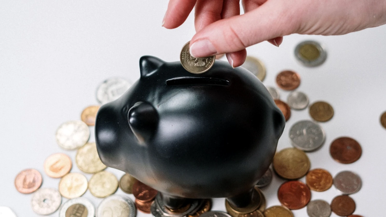 A hand placing a coin into a piggy bank